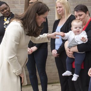 La duchesse Catherine de Cambridge, enceinte de huit mois et vêtue d'un manteau Jojo Maman Bébé, amuse un bébé le 6 mars 2018 lors de sa visite à l'école primaire Pegasus à Oxford pour y observer le travail de l'association Family Links UK.