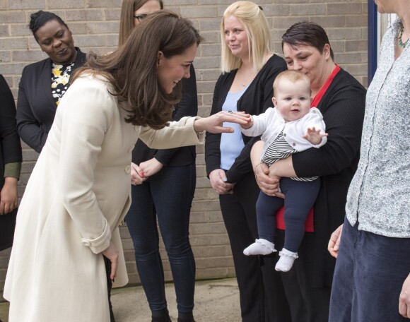 La duchesse Catherine de Cambridge, enceinte de huit mois et vêtue d'un manteau Jojo Maman Bébé, amuse un bébé le 6 mars 2018 lors de sa visite à l'école primaire Pegasus à Oxford pour y observer le travail de l'association Family Links UK.