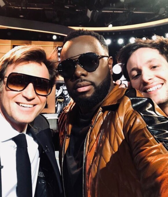 Laurent Delahousse, portant des lunettes de soleil, partage un selfie avec Maître Gims et Vianney sur le plateau de "20h30 le dimanche" sur France 2 le 1er avril 2018.