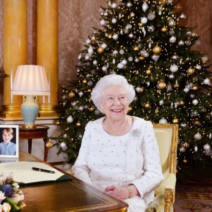 La reine Elizabeth II dans le salon 1844 au palais de Buckingham pour l'enregistrement de son allocution de Noël, le 25 décembre 2017. Sur le bureau à côté d'elle, des photos de George et Charlotte de Cambridge, de son mariage avec le prince Philip et de leurs noces de platine.  Dans la pièce figurait aussi une photo des fiançailles du prince Harry et Meghan Markle.