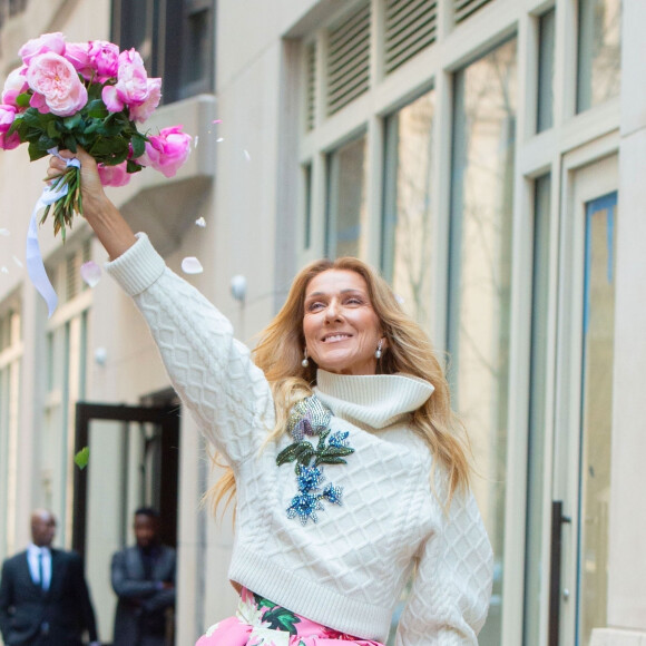 Celine Dion rayonnante et très souriante dans un ensemble pull écru et jupe bouffante fleurie salue ses fans à la sortie de son hôtel à New York, le 8 mars 2020