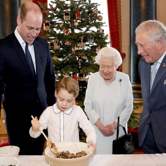 Le prince George de Cambridge prépare, sous le regard bienveillant du prince William, duc de Cambridge, du prince Charles, prince de Galles et de la reine Elisabeth II, des puddings de Noël, dans le cadre du lancement de l'initiative 'Together at Christmas' de la Royal British Legion au Palais de Buckingham, le 21 décembre 2019.