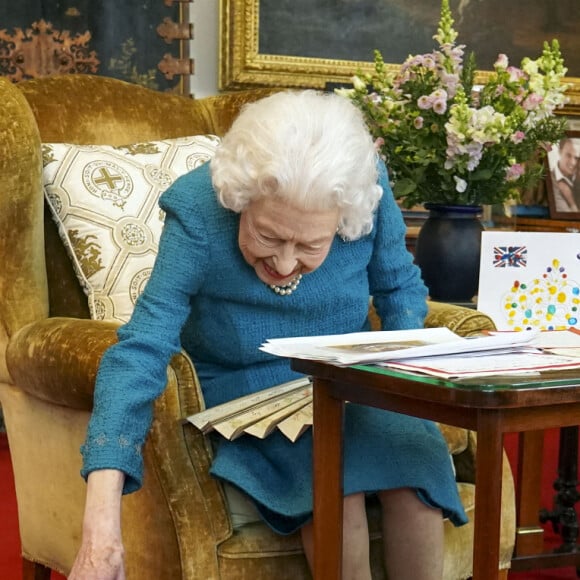 La reine Elisabeth II est rejointe par l'un de ses chiens, un Dorgi appelé Candy, alors qu'elle regarde une exposition de souvenirs de ses jubilés d'or et de platine dans la salle Oak du château de Windsor. Février 2022.