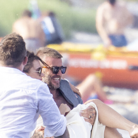 David Beckham et sa femme Victoria quittent la plage des Salins après avoir passé l'après-midi dans une résidence privée à Saint-Tropez le 23 juillet 2022. En grand gentleman, David prend sa femme dans les bras pour monter dans l'annexe du yacht ancré dans la baie pour éviter que sa belle ne mettre les pieds dans les algues échouées au bord de l'eau.