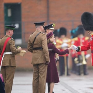 Lady Ghika, l'épouse du lieutenant-colonel régimentaire, le général de division Sir Christopher Ghika, s'avance pour présenter le trèfle à leur mascotte, Seamus, un lévrier irlandais de 3 ans, sur la place du défilé de la caserne de Mons, à Aldershot, lors d'une fête de la Saint-Patrick.