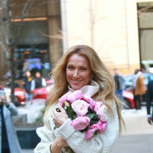 Celine Dion rayonnante et très souriante dans un ensemble pull écru et jupe bouffante fleurie salue ses fans à la sortie de son hôtel à New York, le 8 mars 2020