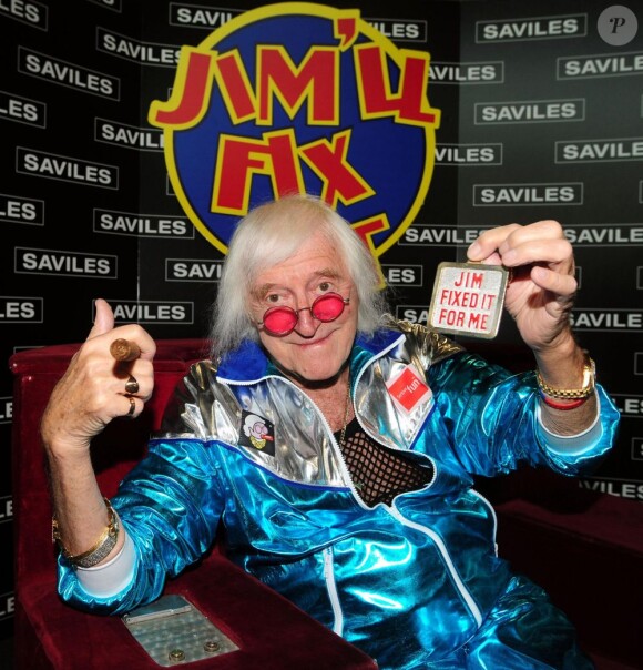 Sir Jimmy Savile devant le logo du fameux Jim'll Fix It chair, cigare cubain et survêtement de sortie en mai 2009.