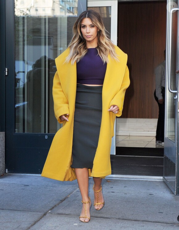 Kim Kardashian sort de l'appartement de son fiancé Kanye West à New York, habillée d'un manteau jaune en laine et angora Max Mara (collection automne-hiver 2013), d'un crop top violet, d'une jupe moulante Lanvin et de sandales Tom Ford. Le 20 novembre 2013.