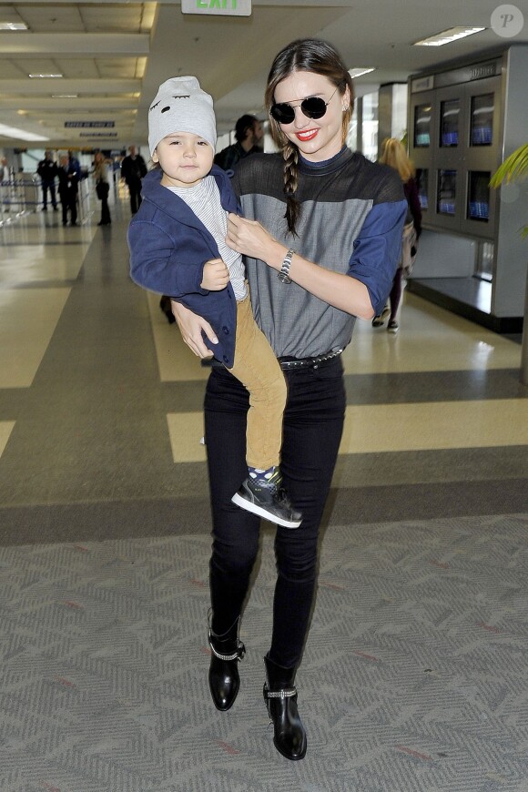 Miranda Kerr et son fils Flynn arrivent à l'aéroport de Los Angeles. Le top model porte des lunettes Prada, un slim noir, une ceinture et des bottines Saint Laurent. Le 20 novembre 2013.