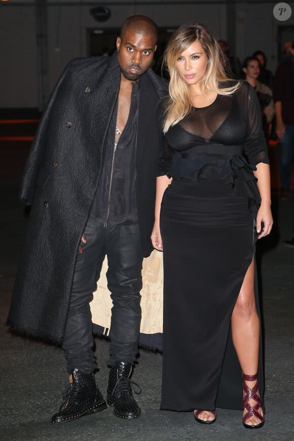 Kanye West et Kim Kardashian lors du défilé Givenchy prêt-à-porter printemps-été 2014à la Halle Freyssinet. Yeezus porte un blazer Rick Owens sous un épais manteau, un pantalon Boris Bidjan Saberi et des bottines Givenchy (pré-collection automne 2013). Paris, le 29 septembre 2013.