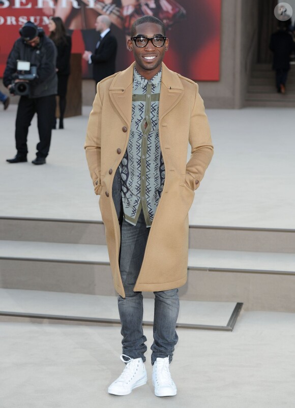 Tinie Tempah assiste au défilé automne-hiver 2013-2014 de Burberry Prorsum, vêtu d'un manteau et d'une chemise (collection printemps-été 2013) de la marque britannique. Londres, le 18 février 2013.