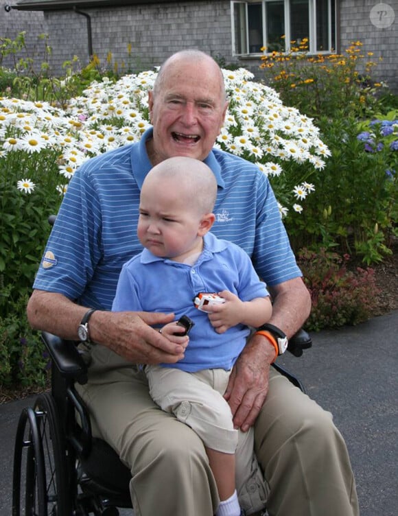 George H. W. Bush prend la pose avec Patrick (2 ans), fils de l'un de ses gardes du corps atteint d'une leucémie. En signe de solidarité, il s'est rasé la tête, comme une vingtaine d'agents de son service de sécurité, le 24 juillet 2013 à Kennebunkport.