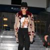 Rita Ora à l'aéroport LAX à Los Angeles, porte un chapeau Maison Michel, un manteau en fourrure Tommy Hilfiger (collection printemps-été 2015), un t-shirt Supreme, un pantalon noir et des bottines Marni. Le 9 décembre 2014.