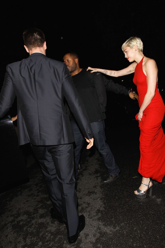 Miley Cyrus dans une belle robe rouge s'accroche à son garde du corps alors qu'elle quitte le bar à cocktails Hooray Henry's à Los Angeles avec son petit copain Patrick Schwarzenegger, le 7 février 2015.