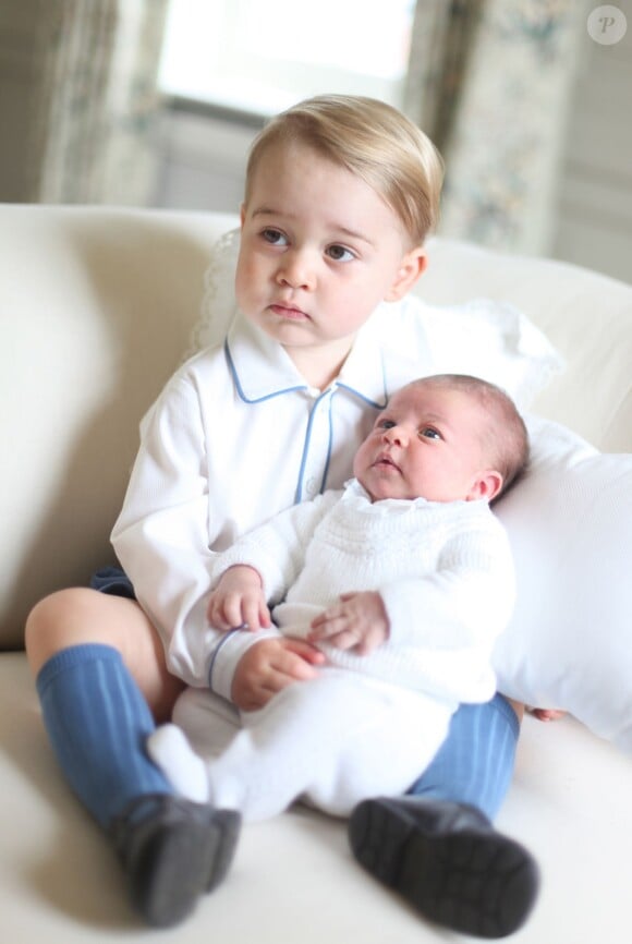 Le prince George de Cambridge avec sa petite soeur la princesse Charlotte dans les bras deux semaines après sa naissance, en mai 2015, photographiés dans leur maison de campagne d'Anmer Hall par leur mère la duchesse Catherine de Cambridge.