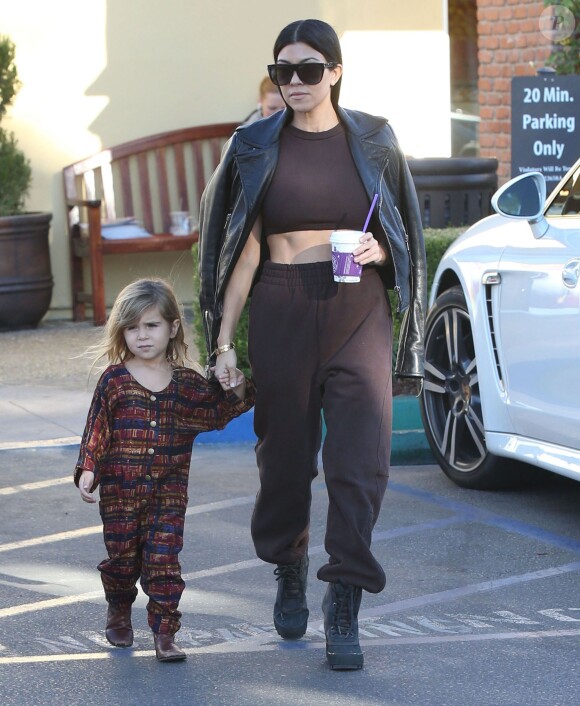 Kourtney Kardashian, photographiée avec sa fille Penelope, porte des lunettes de soleil Céline, un perfecto Balenciaga et un crop top, un jogging et des bottes (modèle Yeezy Boost 950) YEEZY x adidas Originals. Calabasas, le 1er décembre 2015