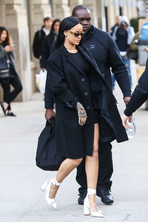 Rihanna se rend au Barclays Center à Brooklyn, habillée d'un manteau et d'une robe noirs, et chaussée de sandales Christian Dior (prêt-à-porter printemps-été 2016). Le 30 mars 2016.