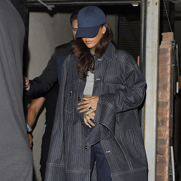Rihanna quitte le Tape à Londres, habillée d'une veste rayée Matthew Adams Dolan, d'un crop top gris, d'un pantalon également rayé Jacquemus et de chaussures Chanel (collection Métiers d'Art Paris-Rome). Une casquette Club 75 accessoirise sa tenue. Le 24 juin 2016.