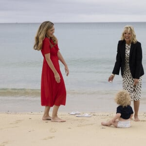 Carrie Johnson s'entretient avec la Première Dame des États-Unis, Jill Biden, lors du sommet des dirigeants du G7 à Carbis Bay, Royaume Uni, le 10 juin 2021, alors que Wilfred Johnson est assis sur la plage.