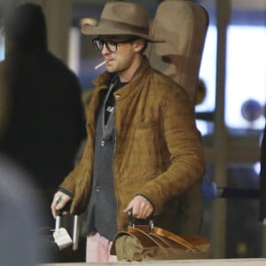Tom Felton arrive à l'aéroport de Vancouver le 9 janvier 2017. Il porte une guitare sur le dos et une paire de jean rose 