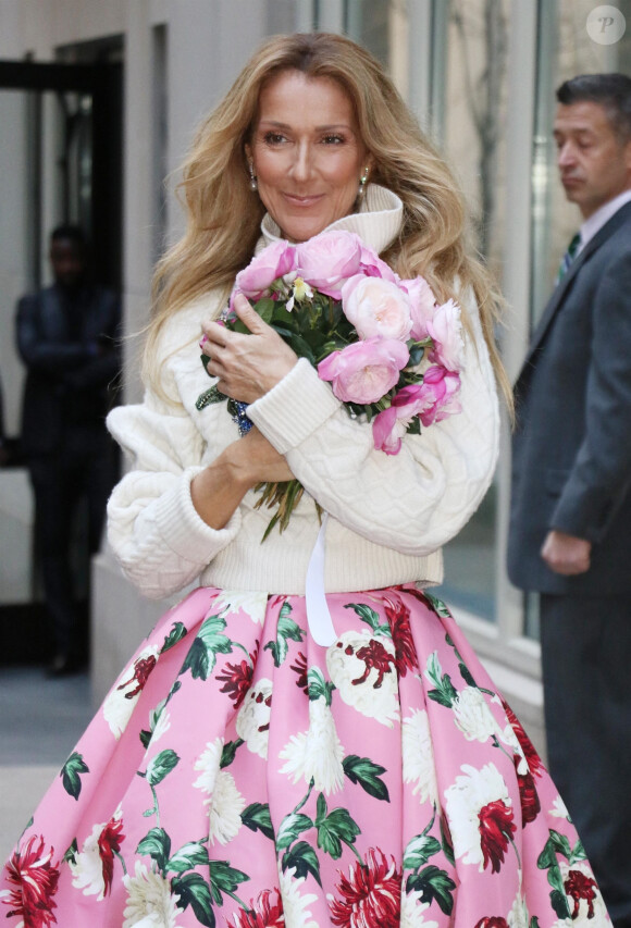 Celine Dion rayonnante et très souriante dans un ensemble pull écru et jupe bouffante fleurie salue ses fans à la sortie de son hôtel à New York, le 8 mars 2020 