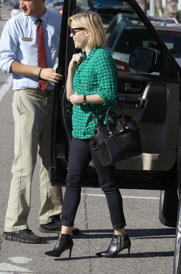 Reese Witherspoon, souriante à Los Angeles, porte des lunettes Ray-Ban Wayfarer, une chemise à carreaux, un sac en bandoulière Reed Krakoff et des bottines noires Saint Laurent. Le 30 novembre 2013.