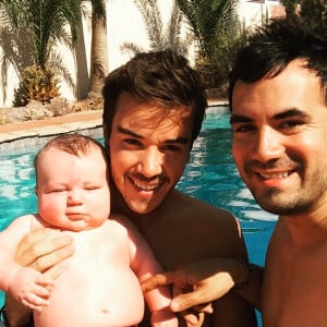 Alex Goude, Romain et leur bébé Elliot posent ensemble dans la piscine. Juin 2015.