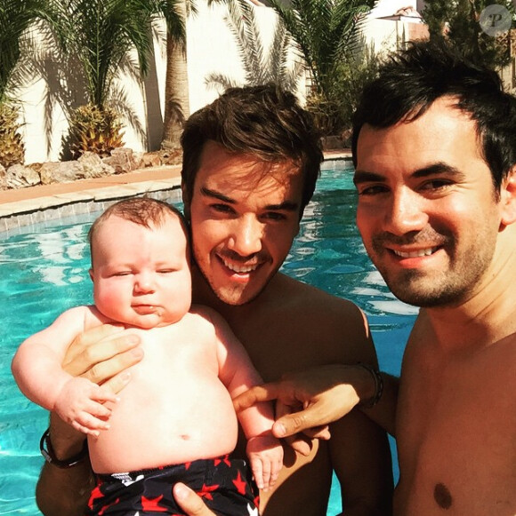 Alex Goude, Romain et leur bébé Elliot posent ensemble dans la piscine. Juin 2015.