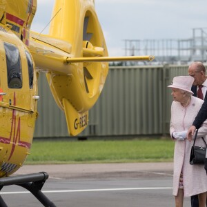 Le pricne William à l'aéroport de Cambridge le 13 juillet 2016, faisant visiter les lieux et découvrir son hélicoptère à la reine Elizabeth II et au duc d'Edimbourg, qui inauguraient les nouveaux locaux d'East Anglia Air Ambulance.