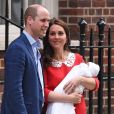  La duchesse Catherine de Cambridge (Kate Middleton), en robe Jenny Packham rappelant la tenue rouge de Lady Diana 34 ans plus tôt dans les mêmes circonstances, avec le prince William et leur troisième enfant à la sortie de l'aile Lindo du St Mary's Hospital le 23 avril 2018. 