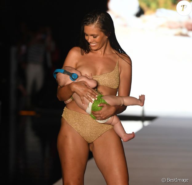 La maman mannequin Mara Martin allaite sa fille Aria, âgée de 5 mois, sur le podium  du défilé Sports Illustrated Swimsuit à la Paraison Fashion Fair à Miami, le 15 juillet 2018.