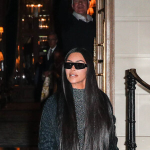 Kim Kardashian quitte le Ritz pour se rendre au restaurant Ferdi, elle porte un long manteau de laine, une combinaison transparente à paillettes argentées et des escarpins à noeuds, Paris, le 25 mars 2019.