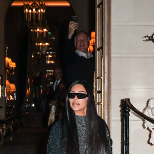 Kim Kardashian quitte le Ritz pour se rendre au restaurant Ferdi, elle porte un long manteau de laine, une combinaison transparente à paillettes argentées et des escarpins à noeuds, Paris, le 25 mars 2019.
