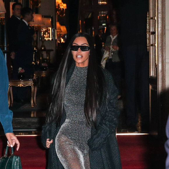 Kim Kardashian quitte le Ritz pour se rendre au restaurant Ferdi, elle porte un long manteau de laine, une combinaison transparente à paillettes argentées et des escarpins à noeuds, Paris, le 25 mars 2019.