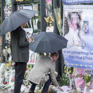 Le prince William et le prince Harry, le 30 août 2017, observant les témoignages d'affection du public à la mémoire de Lady Di sur les grilles du palais de Kensington, à la veille du 20e anniversaire de sa mort.