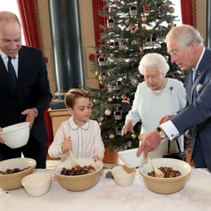 Le prince George de Cambridge prépare, sous le regard bienveillant du prince William, duc de Cambridge, du prince Charles, prince de Galles et de la reine Elisabeth II, des puddings de Noël, dans le cadre du lancement de l'initiative 'Together at Christmas' de la Royal British Legion au Palais de Buckingham, le 21 décembre 2019.