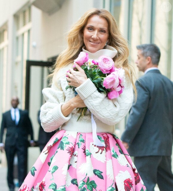 Celine Dion rayonnante et très souriante dans un ensemble pull écru et jupe bouffante fleurie salue ses fans à la sortie de son hôtel à New York, le 8 mars 2020