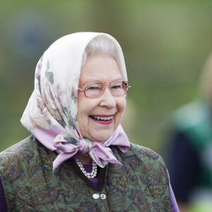 Elizabeth II, vêtue d'un gilet molletonné et de bottes de pluie, assiste à une course hippique.