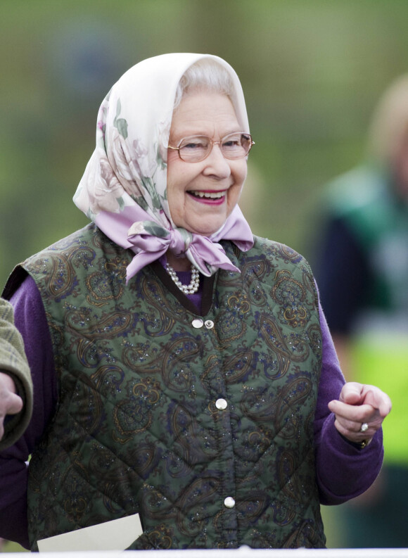 Elizabeth II, vêtue d'un gilet molletonné et de bottes de pluie, assiste à une course hippique.