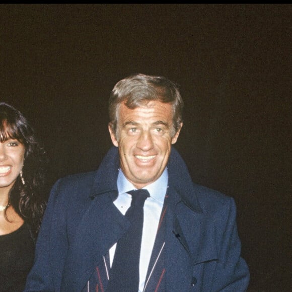 Archives - Jean-Paul Belmondo et sa compagne Carlos Sotto Mayor lors de la générale du spectacle de Thierry Le Luron à Paris. 1983.