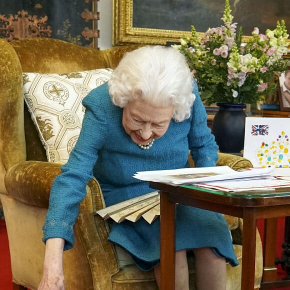 La reine Elisabeth II est rejointe par l'un de ses chiens, un Dorgi appelé Candy, alors qu'elle regarde une exposition de souvenirs de ses jubilés d'or et de platine dans la salle Oak du château de Windsor. Février 2022.