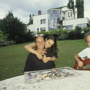 Elles passaient beaucoup de temps en famille avec Guy
Archives -En France, à Garches, chez lui, de gauche à droite, son épouse Cécile Béart, sa fille Eve créatrice de bijoux et Guy Béart jouant de la guitare, tous autour d'une table dans le jardin.