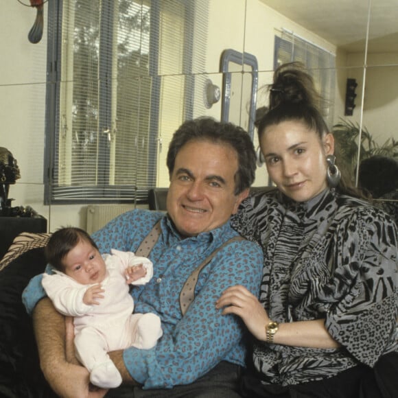 Archives - En France, à Garches, chez lui, Guy Béart tenant dans ses bras Laura, 1 mois 1/2, sa petite-fille, enfant d' Eve, sa fille.