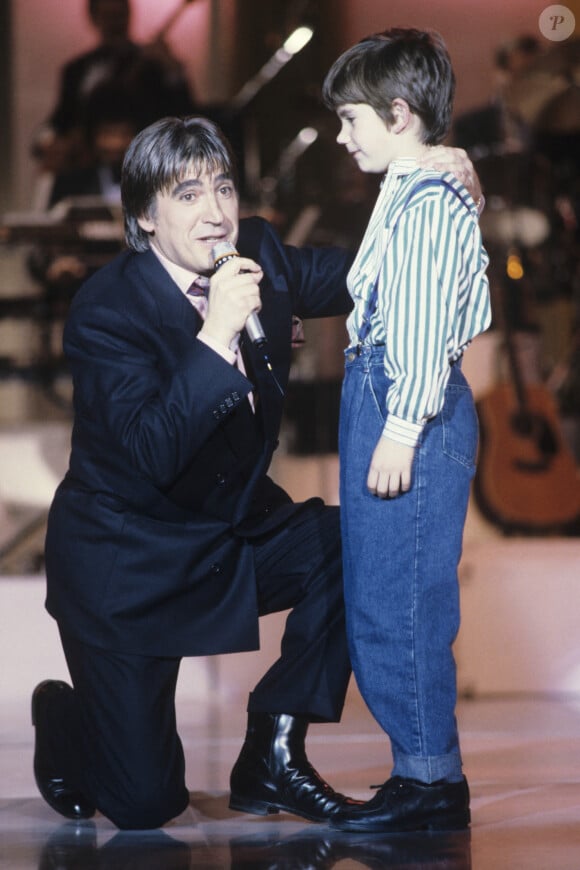 Archive - Serge Lama. En France, à Paris, Serge Lama chantant à genoux devant son fils Frédéric, 9 ans, sur un plateau de télévision.