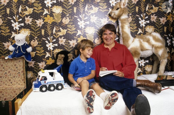 Archive - Serge Lama. En France, à Paris, en intérieur, Serge Lama et son fils Frédéric, 6 ans, tous deux assis sur le lit dans la chambre de l'enfant, entourés de ses jouets.