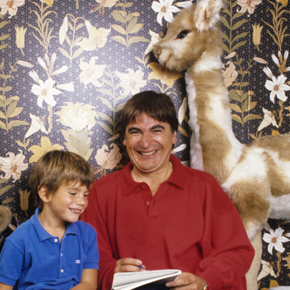 Archive - Serge Lama. En France, à Paris, en intérieur, Serge Lama et son fils Frédéric, 6 ans, tous deux assis sur le lit dans la chambre de l'enfant, entourés de ses jouets.