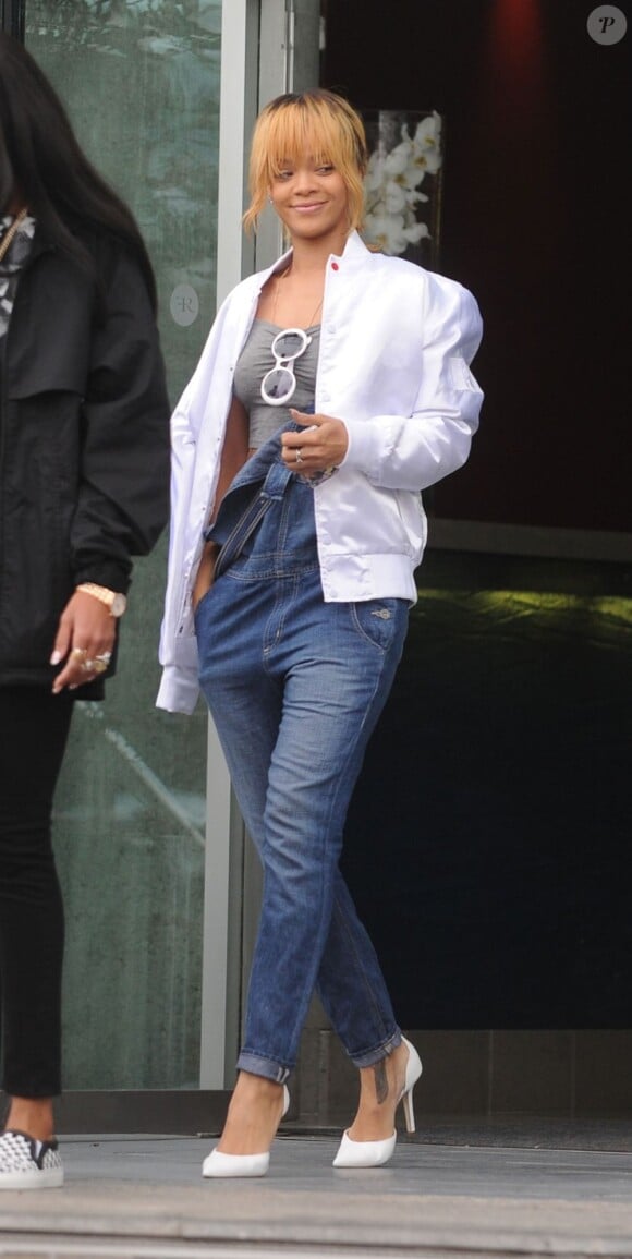 Rihanna quitte l'hôtel Lowry à Manchester, vêtue d'un bomber Trapstar, d'un top gris Rihanna for River Island avec ses lunettes Chanel accrochées, d'une salopette Big Star USA et de souliers Manolo Blahnik. Le 12 juin 2013.
