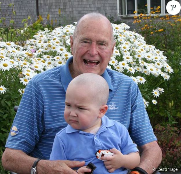 George H. W. Bush prend la pose avec Patrick (2 ans), fils de l'un de ses gardes du corps atteint d'une leucémie. En signe de solidarité, il s'est rasé la tête, comme une vingtaine d'agents de son service de sécurité, le 24 juillet 2013 à Kennebunkport.