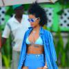 Rihanna, sublime sur une plage de la Barbade, porte des lunettes Le Specs (modèle The Dandy), une chemise en jean, un bikini Charlie by MZ, un sac à main noir vernis Louis Vuitton (modèle Alma BB) et des baskets Converse. Le 26 décembre 2013.