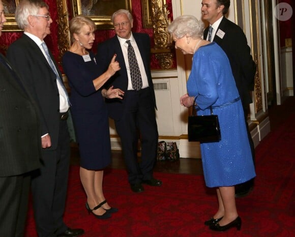 La reine Elizabeth II écoute Dame Helen Mirren, index brandi, qui lui raconte son moment avec le prince William aux BAFTA Awards la veille, lors de la réception organisée le 17 février 2014 à Buckingham Palace pour célébrer les soixante ans du patronage de la Royal Academy of Dramatic Art par la reine Elizabeth II.